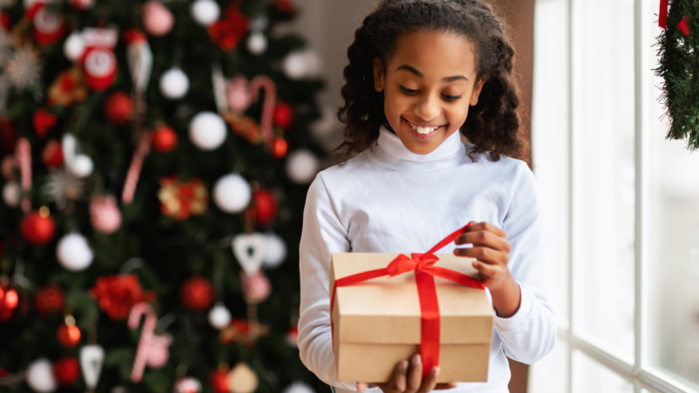 jeune fille footballeuse avec un grand sourire qui ouvre un cadeau devant un sapin de noël