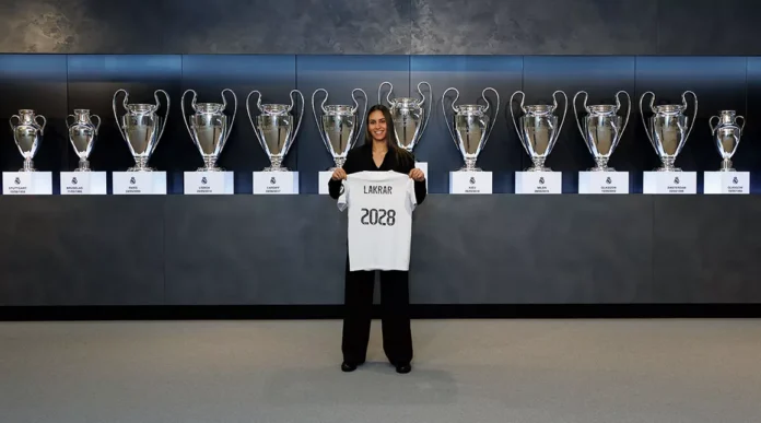 La joueuse de football française Maëlle Lakrar se tient devant une exposition de trophées du Real Madrid avec un maillot portant le nombre 2028 ce qui correspond à la date de sa prolongation