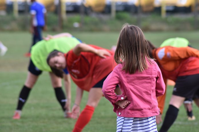 petite fille de dos qui regarde des joueuses de football s'échauffer sur un terrain de foot