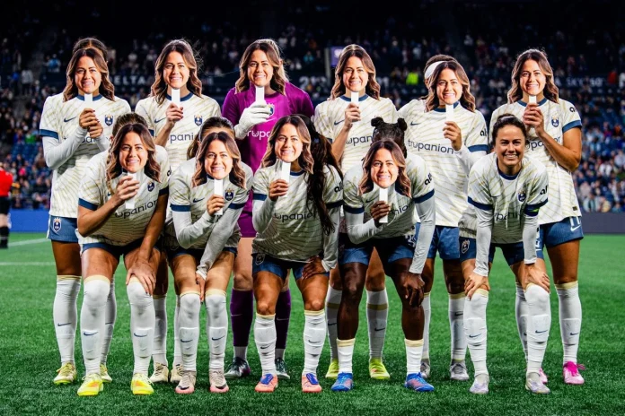 Cette image montre l'équipe féminine de soccer Seattle Reign FC portant des masques de leur coéquipière Lauren Barnes pour célébrer son dernier match à domicile